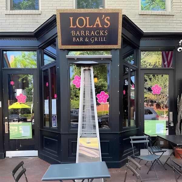 Lola's Barracks Bar & Grill storefront with outdoor seating, a patio heater, and pink flower decals.