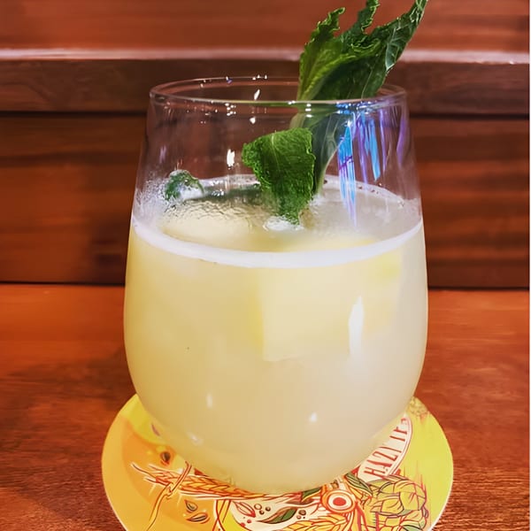 A refreshing yellow cocktail with mint garnish and ice, on a colorful coaster at Lola's.
