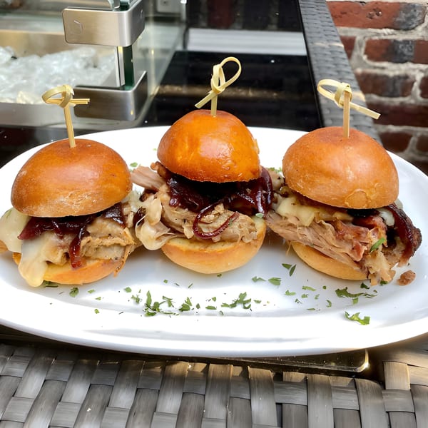 Three Lola's pulled pork sliders with melted cheese and caramelized onions on a white plate.