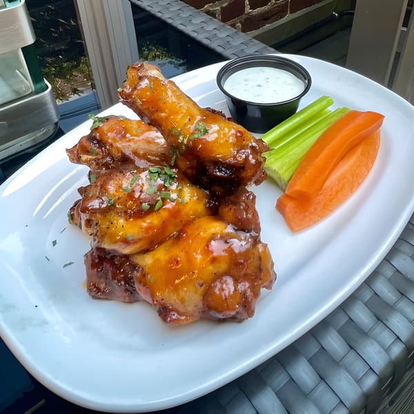 Sweet and spicy chicken wings with ranch, celery, and carrots on a white plate.